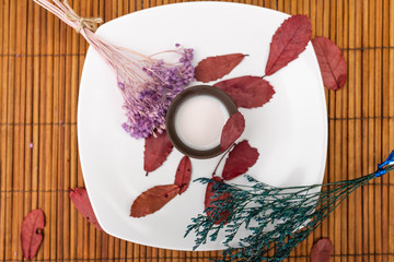 A white plate located on the mat on which stands a clay cup with milk and a sprig of lavender and red tree petals.