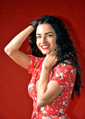 Beautiful smiling woman with gorgeous smile and cute face. Pretty girl with a long dark hair in a red dress. Female portrait. Beauty. Close up. Red background