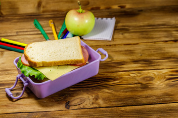 Back to school concept. School supplies, apple and lunch box with sandwiches on a wooden desk