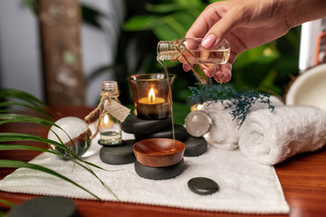 Fototapeta na wymiar A girl pours oil from a jar of aromatic oils standing on stones for stone therapy and located on a terry towel next to which are transparent spheres, a twisted towel and a sprig of lavender