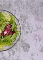 Salad. Organic food. Healthy vegetable salad with escarole endive, frisee endive, chicory radicchio, lettuce in a glass bowl. Gray table top background. Top view. Vegetarian food.