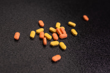 A handful of yellow and orange pills on a black background.Health concept. The concept of pharmacology.