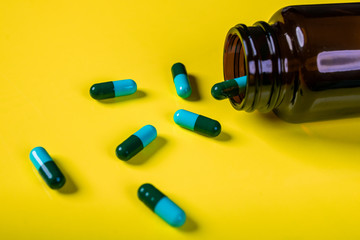 Blue-green capsules poured from a brown medicine jar on a yellow background.The concept of pharmacology.