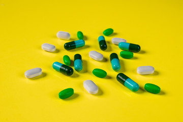 Capsules of white and blue-green color scattered on a yellow background.The concept of pharmacology.