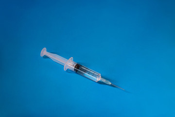 One syringe with the collected medicine located in the center on a blue background.Health concept.