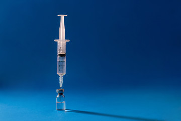 One syringe inserted into the ampoule with the drug located to the left of the center on a blue background. Medicine concept.