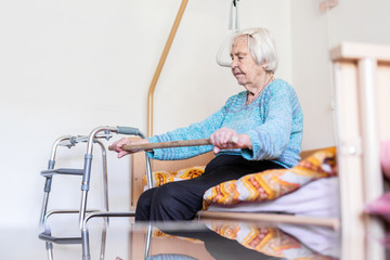 Elderly 96 years old woman exercising with a stick sitting on her bad. Geriatric health care home...