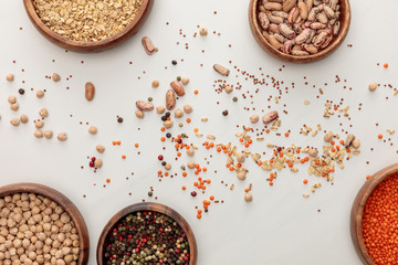 top view of wooden plates with chickpea, lentil, peppercorns, oatmeal and beans near scattered...