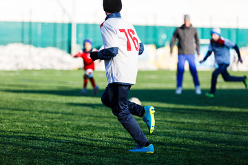 Boys in white and red sportswear plays  football on field, dribbles ball. Young soccer players with ball on green grass. Training, football, active lifestyle for kids , winter sport