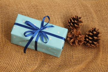 gift in a cardboard box tied with a blue satin ribbon, beautiful pine cones on a natural burlap, top view, copy space
