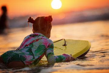 golden waves of wonderful sea splashing near adorable girl in swimsuit carrying yellow surfboard on...