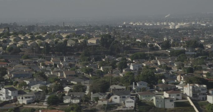 Aerial shot, day, tree populated la neighborhoodin foreground, smoke pumping industrial sector in background, drone