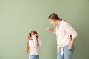 Angry mother scolding her little daughter on color background