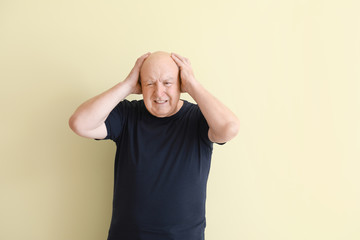 Senior man suffering from headache on light background