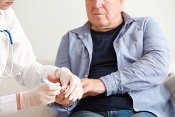Doctor taking blood sample of diabetic man in clinic