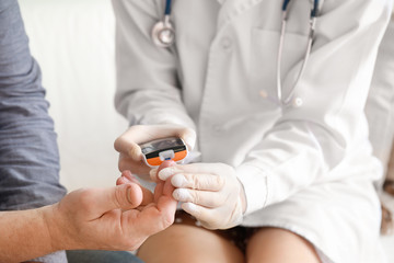 Doctor checking blood sugar level of diabetic patient in clinic, closeup