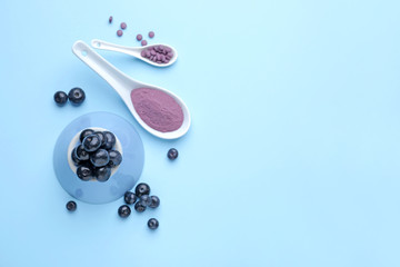 Fresh acai berries with powder and tablets on color background