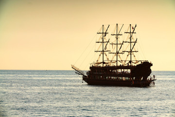 Obraz premium old pirate ship sailing at sea sunset