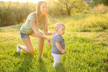 Mother teaching her little baby to walk outdoors