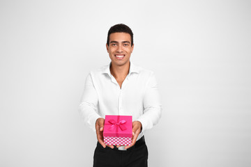 Handsome African-American man with gift on white background