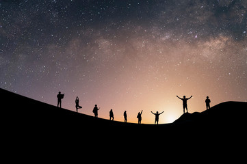 Naklejka na ściany i meble Silhouette group of tourists watch the view of star and milky way on the top of the mountain and raise their hands pointing to the stars before sunrise. We are happy to be with herself and nature.