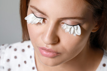 Young woman with creative eyelashes on grey background, closeup