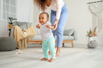 African-American mother teaching her little baby to walk at home