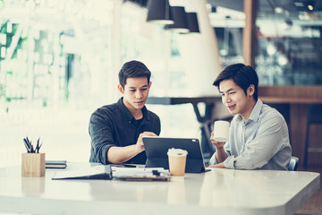 Young Asian businessmen using a digital tablet to discuss information in a modern business working space.