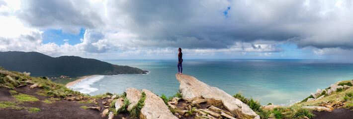 Panorámica de mujer en la cima de una montaña observando un mar y su playa con montañas verdes de fondo