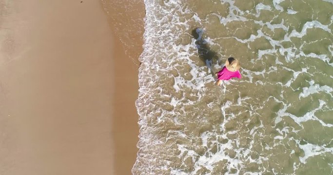 Mujer que pasea en la orilla de playa dorada y un dron vuela vista cenital