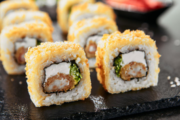 Macro shot of hot crispy ebi tempura maki sushi rolls with cream cheese, king prawn, chuka kelp salad and nori. Deep fried uramaki roll set on natural black stone slate background closeup © Ryzhkov