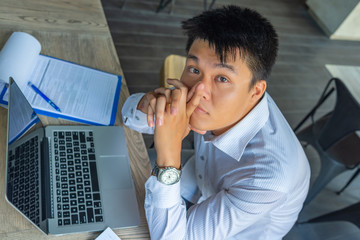 Young Asian businessman sitting with laptop and paperworks at office
