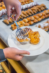 Human picking assorted pastry into white plate at buffet party