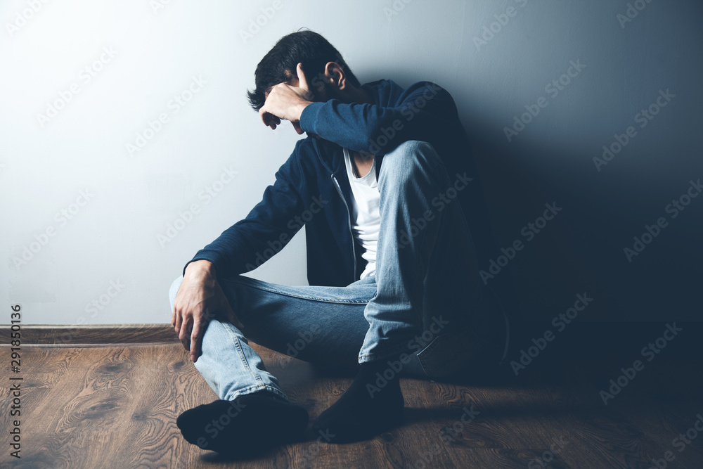 Wall mural sad man sitting on ground on dark background