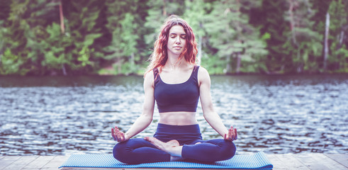 Beautiful girl in a yoga pose on the lake. Lotus position ,  Padmasana. The concept of appeasement,  healthy lifestyle. Panoramic view