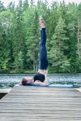 Young yogi  girl  practicing yoga, standing in Salamba Sarvangasana exercise, supported Shoulder stand pose on the lake.  Concept of healthy life and natural balance