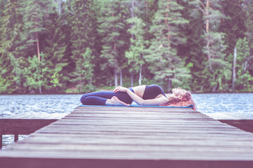 Young yogi  girl  practicing yoga, Reclining Hero exercise, Virasana pose on the lake. The concept of appeasement,  healthy lifestyle.