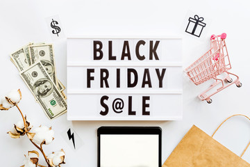 Creative promotion composition Black friday sale text on lightbox on white background, next grocery trolley, credit card, cash money, mobile phone, shopping bag. Flat lay, top view, overhead, mockup