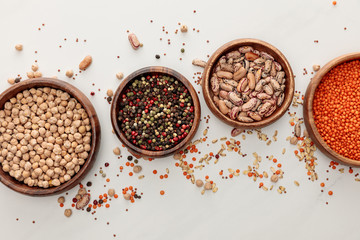 top view of wooden plates with chickpea, lentil, peppercorns, and beans near scattered grains on...
