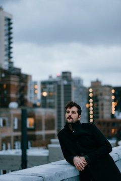 Portrait of man with black raincoat on a roof next to some buildings