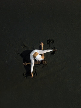 Woman doing yoga exercices on a black beach