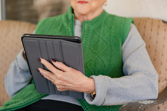A mature woman sitting on her patio, using her tablet device.