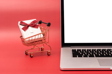 Laptop and shopping cart model with gifts on red background
