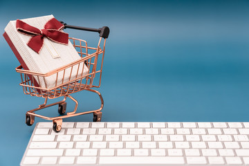 Keyboard and shopping cart model with gifts on blue background