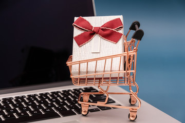 Laptop in front of blue background and shopping cart model with gifts