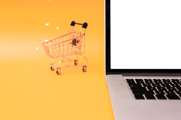 Shopping cart model and laptop on yellow background