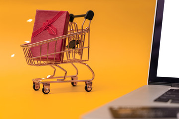 Shopping cart model and computer with gifts in front of yellow background