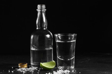 Vodka in shot glass and mini bottle on black background with a blank space for a text, Russian vodka with salt and lemon
