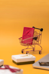 Shopping cart model and computer with gifts in front of yellow background