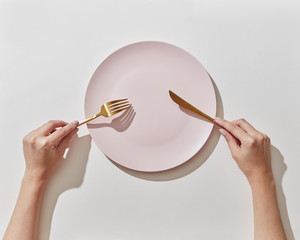Waiting for oder dinner with served plate, fork and knife in a girl's hands on a white background. Place for text, top view.